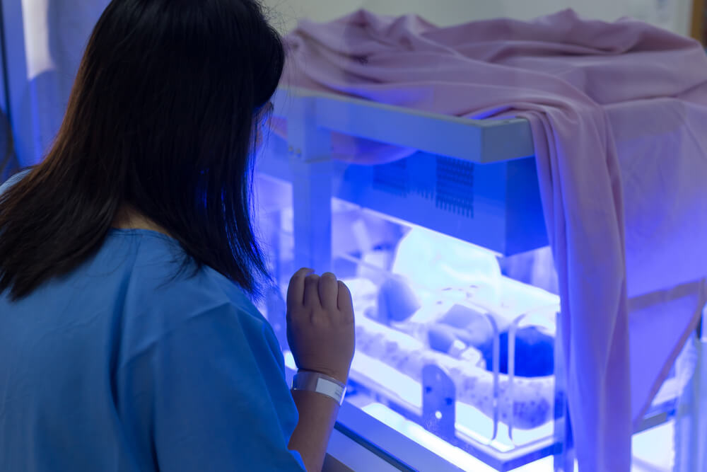 Majka koja gleda svoje novorođenče pod UV svijetlom